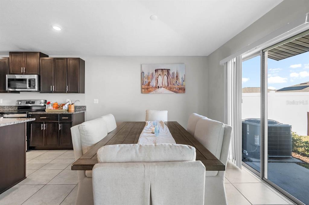 A dining area features a wooden table with upholstered chairs, dark cabinets, and sliding glass doors — 889 CALICO SCALLOP STREET, RUSKIN, FL
