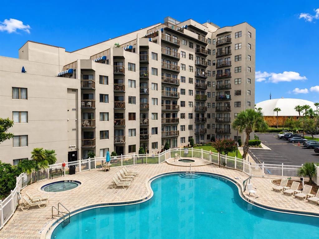 An outdoor swimming pool and hot tub are situated in front of a multi-story apartment building — 6165 CARRIER DRIVE UNIT 2305, ORLANDO, FL