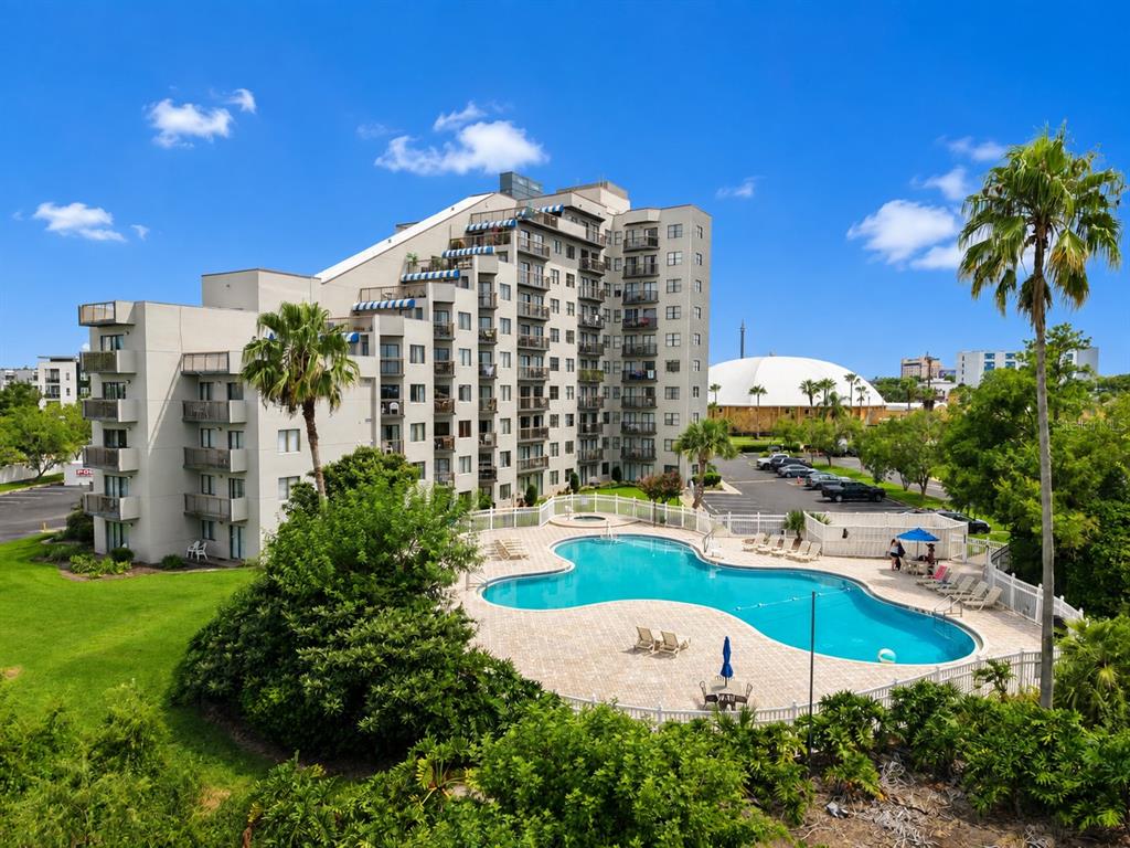 An aerial view shows a multi-story apartment building with a swimming pool and palm trees — 6165 CARRIER DRIVE UNIT 2305, ORLANDO, FL