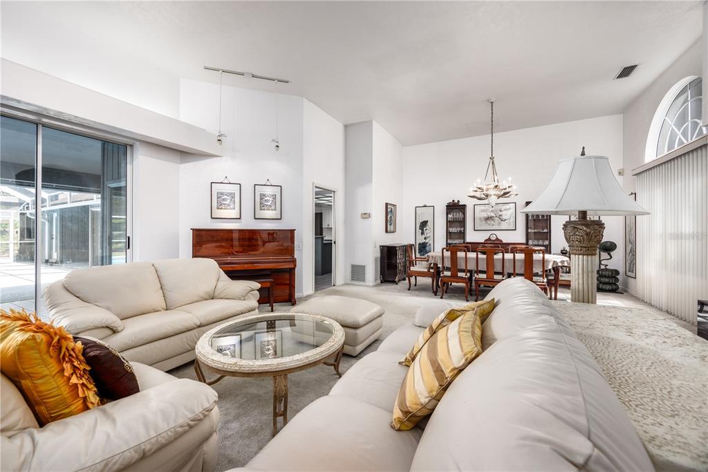 A living room with white sofas, a glass coffee table, a piano, and dining area — 4616 NW 57TH DRIVE, GAINESVILLE, FL