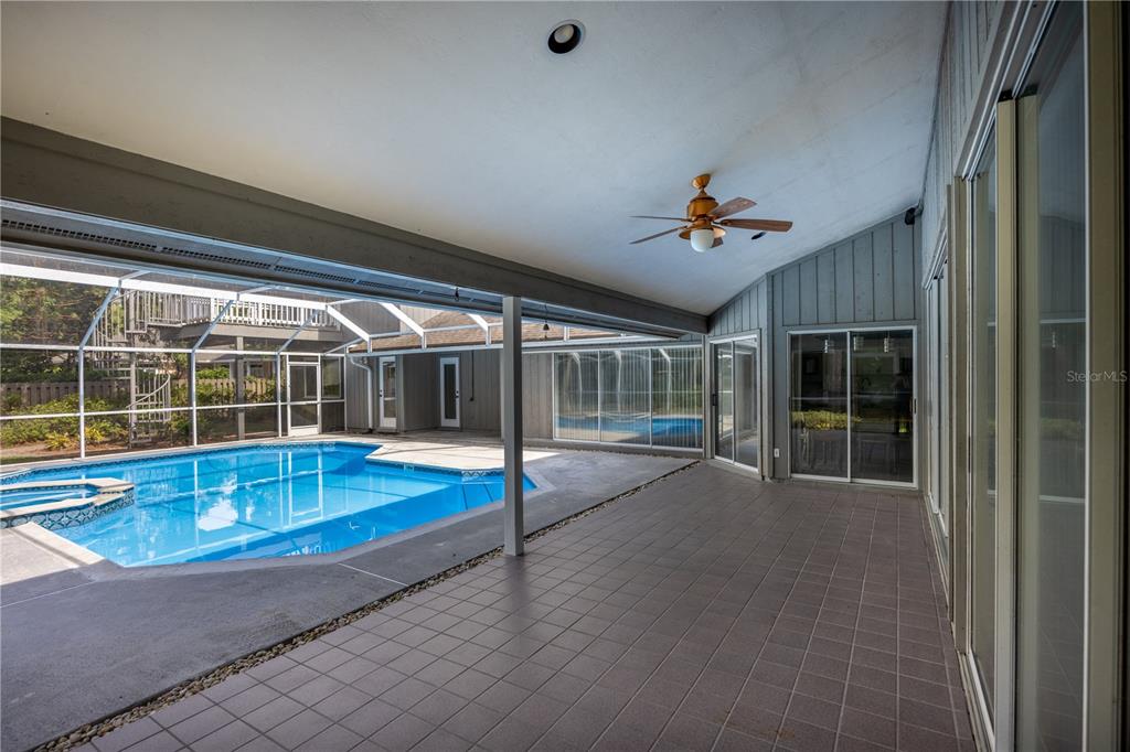 A covered patio with tiled flooring overlooks a swimming pool enclosed by a screen cage — 4616 NW 57TH DRIVE, GAINESVILLE, FL