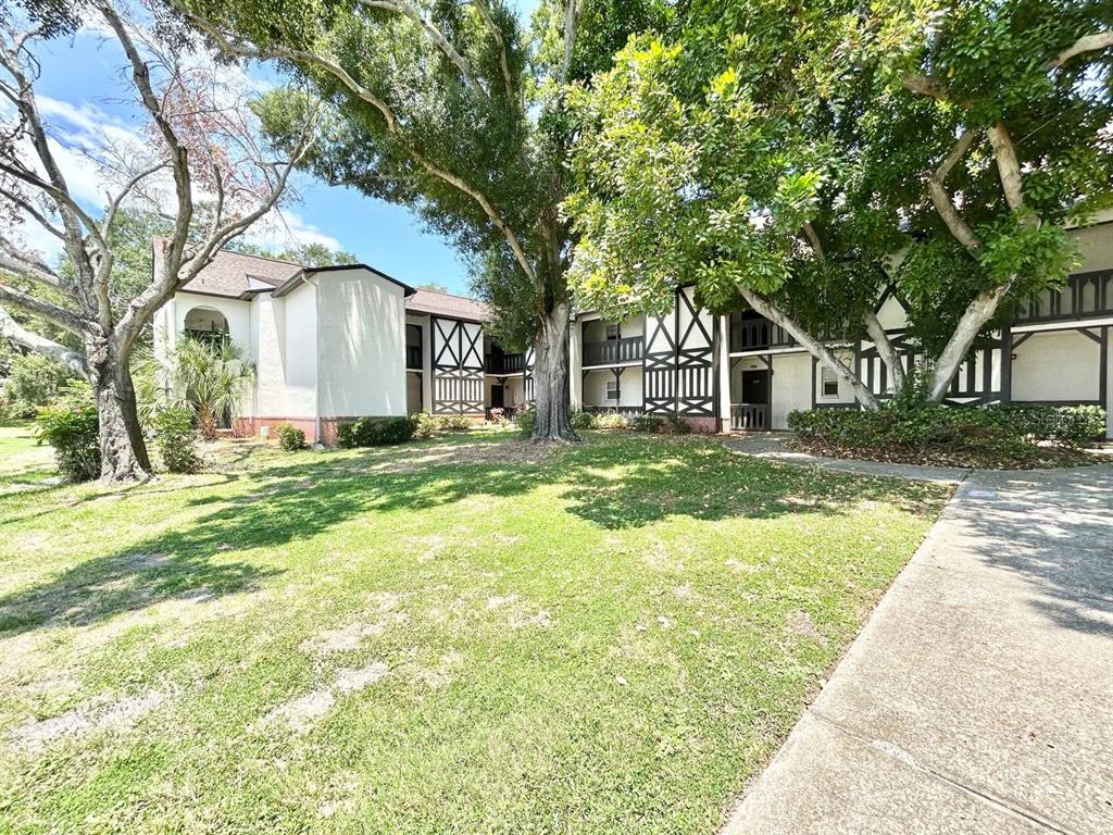A two-story apartment building with Tudor-style trim sits behind a grassy lawn and trees — 420 N BAYSHORE BOULEVARD UNIT 102, CLEARWATER, FL