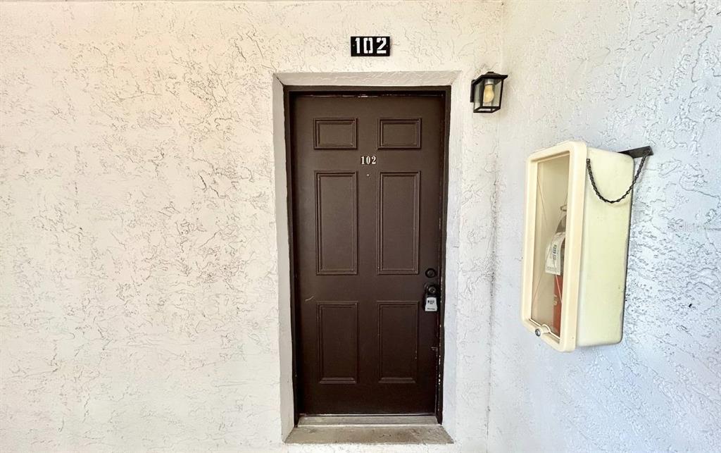 A brown front door labeled 102 is set into a white textured exterior wall — 420 N BAYSHORE BOULEVARD UNIT 102, CLEARWATER, FL