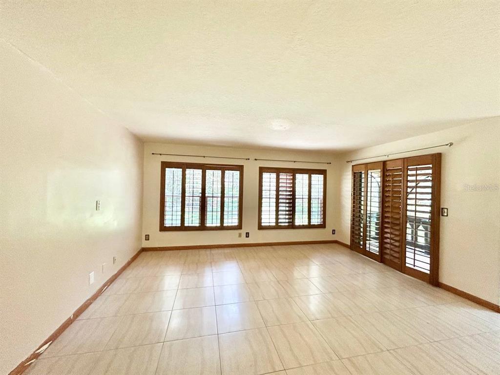 A bright, empty living room features light-colored tile flooring, large windows with shutters, and sliding doors — 420 N BAYSHORE BOULEVARD UNIT 102, CLEARWATER, FL