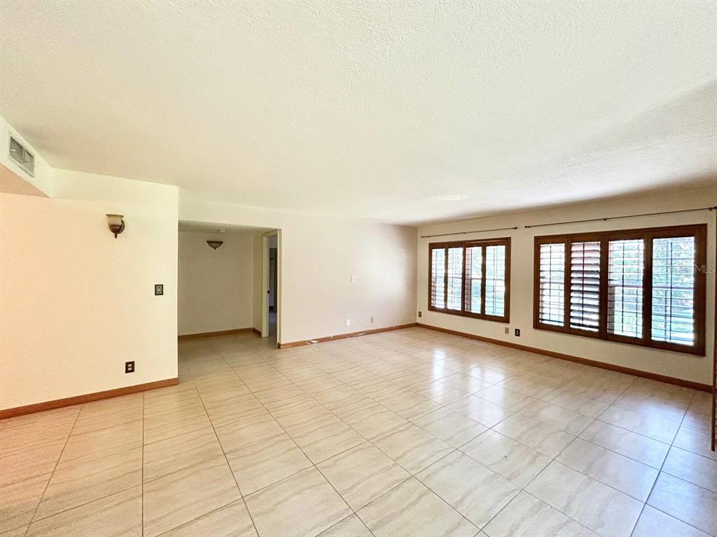 An empty living room features light-colored tile flooring, white walls, and large windows with shutters — 420 N BAYSHORE BOULEVARD UNIT 102, CLEARWATER, FL