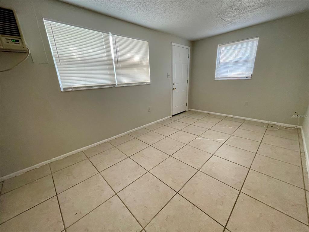 A room with light-colored tile flooring, beige walls, a window air conditioner, and a door — 9803 N 11TH STREET UNIT B, TAMPA, FL