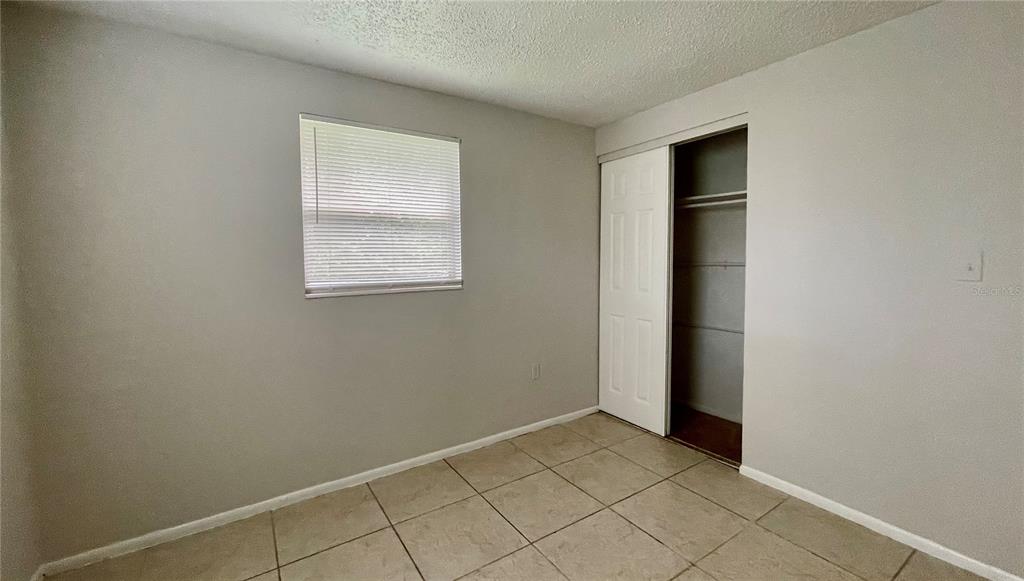 An empty bedroom features light gray walls, tile flooring, a window with blinds, and a closet — 9803 N 11TH STREET UNIT B, TAMPA, FL
