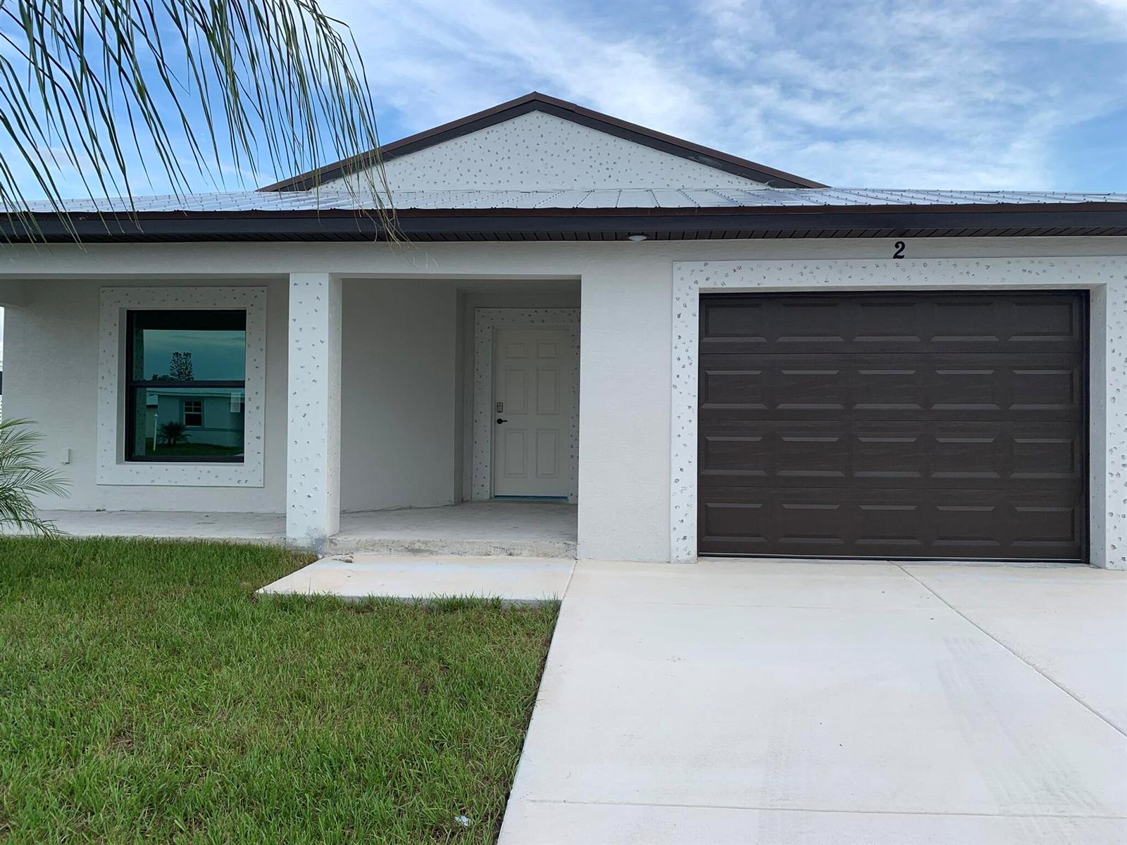 A single-story house features a white exterior, a dark garage door, and a metal roof — 43 La Villa Way, Fort Pierce FL 34951, FORT PIERCE, FL