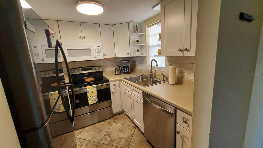 A kitchen features white cabinets, stainless steel appliances, a double sink, and tiled flooring — 5154 TURQUOISE LANE UNIT 201, NEW PORT RICHEY, FL
