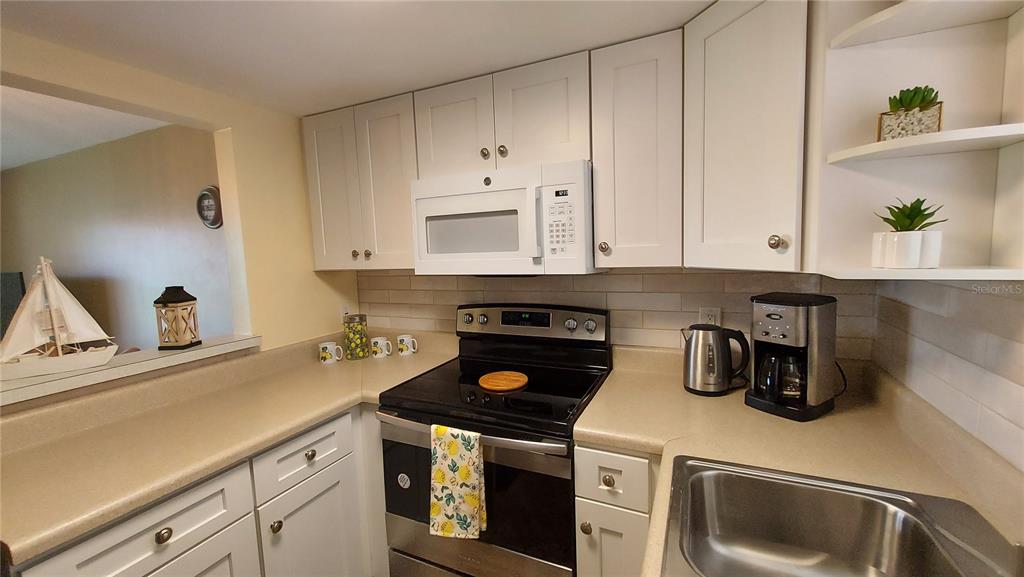 A kitchen features white cabinets, a black stove, a microwave, and a stainless steel sink — 5154 TURQUOISE LANE UNIT 201, NEW PORT RICHEY, FL