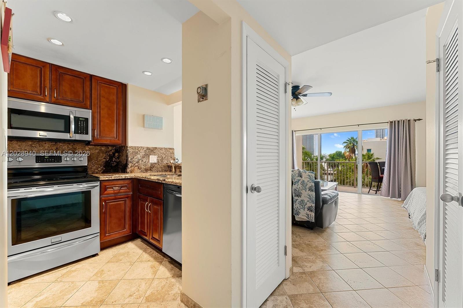 A kitchen with wood cabinets and stainless appliances opens into a living area with balcony — 1965 S Ocean Dr # 3L, Hallandale Beach FL 33009, HALLANDALE BEACH, FL