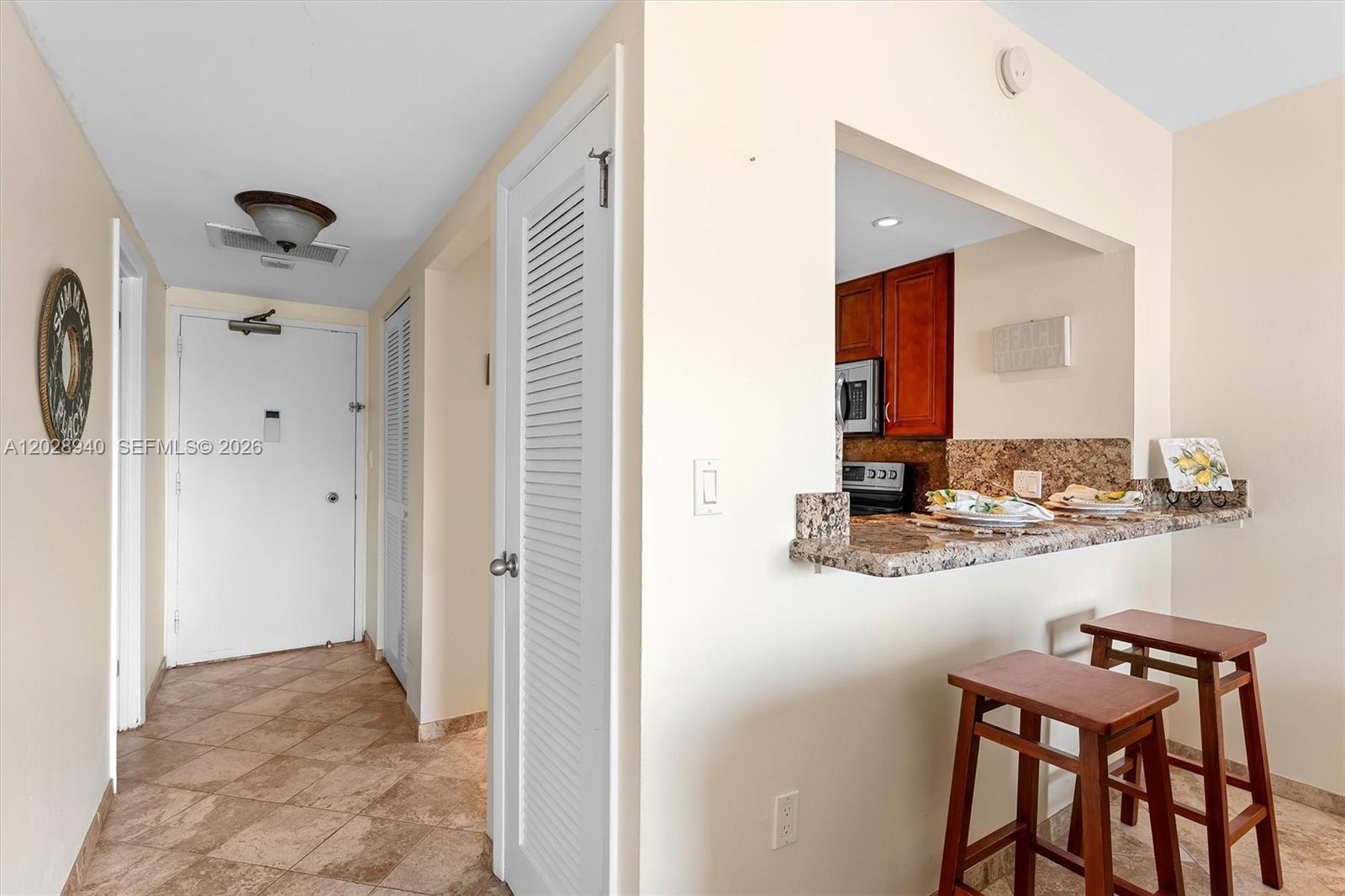 A hallway with tiled floors leads to a kitchen featuring a granite breakfast bar — 1965 S Ocean Dr # 3L, Hallandale Beach FL 33009, HALLANDALE BEACH, FL