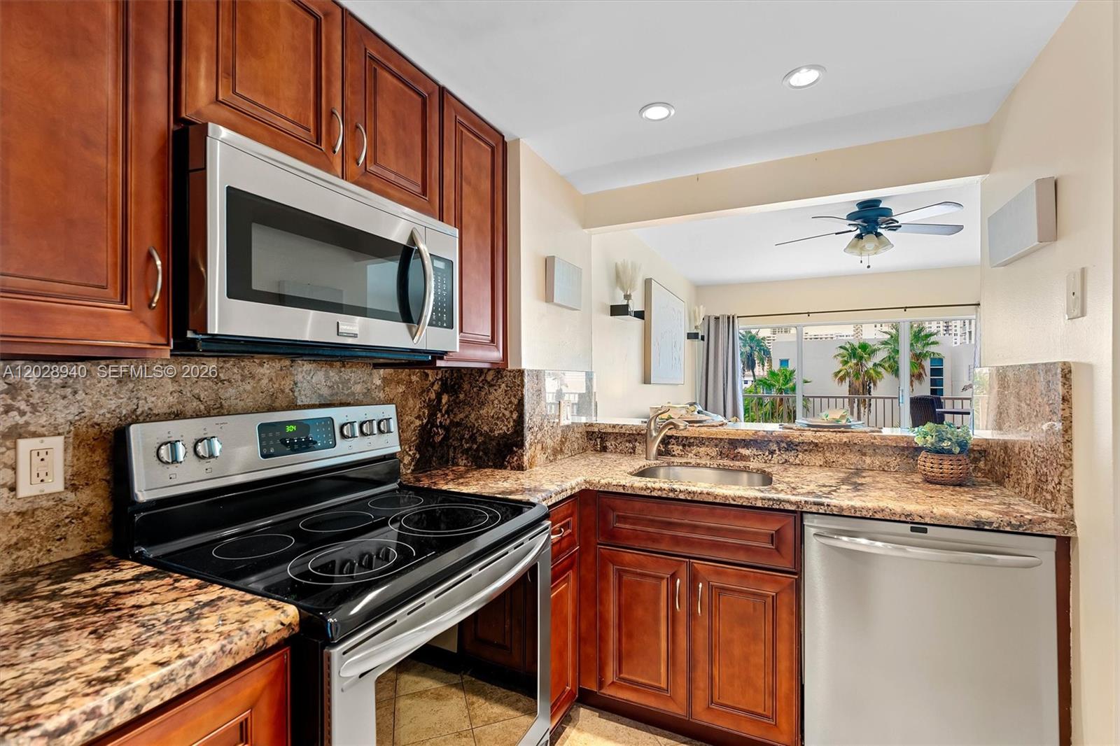 A kitchen features cherry wood cabinets, granite countertops, stainless steel appliances, and a pass-through window — 1965 S Ocean Dr # 3L, Hallandale Beach FL 33009, HALLANDALE BEACH, FL
