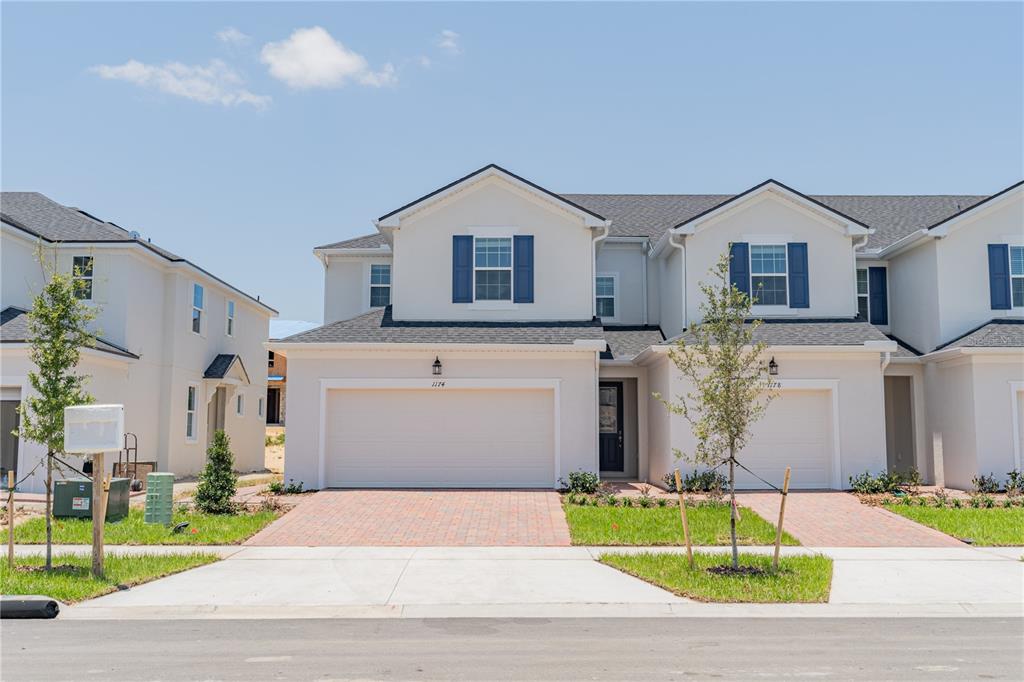 A two-story townhouse with a white stucco exterior, blue shutters, and a two-car garage — 1174 SEASIDE MIST TRAIL, KISSIMMEE, FL