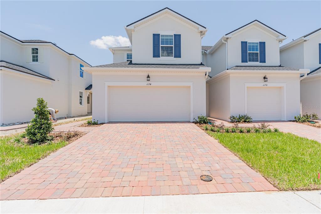 A two-story house with a white exterior, blue shutters, and a brick paver driveway — 1174 SEASIDE MIST TRAIL, KISSIMMEE, FL