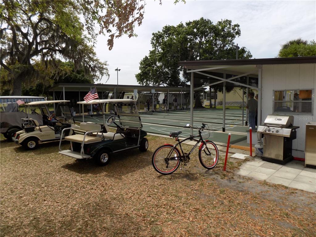 A golf cart, a bicycle, and a grill sit outside a covered shuffleboard court area — 6849 ALANI COURT, NORTH PORT, FL