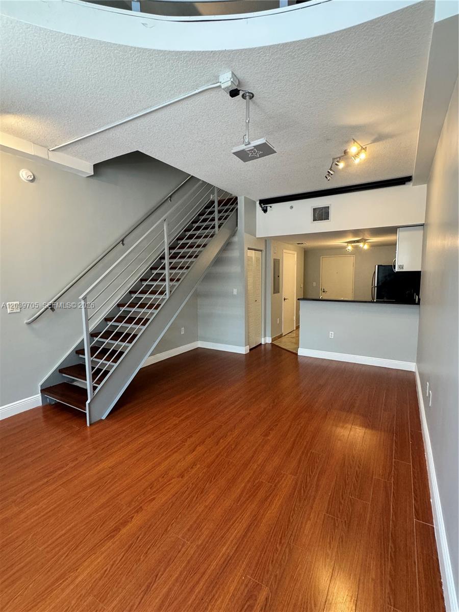 An open living area features wood-look flooring, a metal staircase, and a kitchen pass-through — 3339 Virginia St # 105, Miami FL 33133, MIAMI, FL