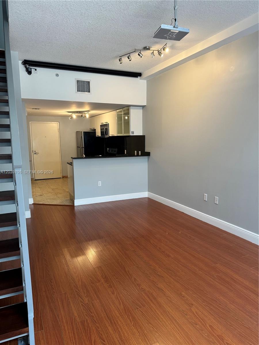 An open-concept living area features wood-look flooring, a staircase, and an adjacent kitchen — 3339 Virginia St # 105, Miami FL 33133, MIAMI, FL