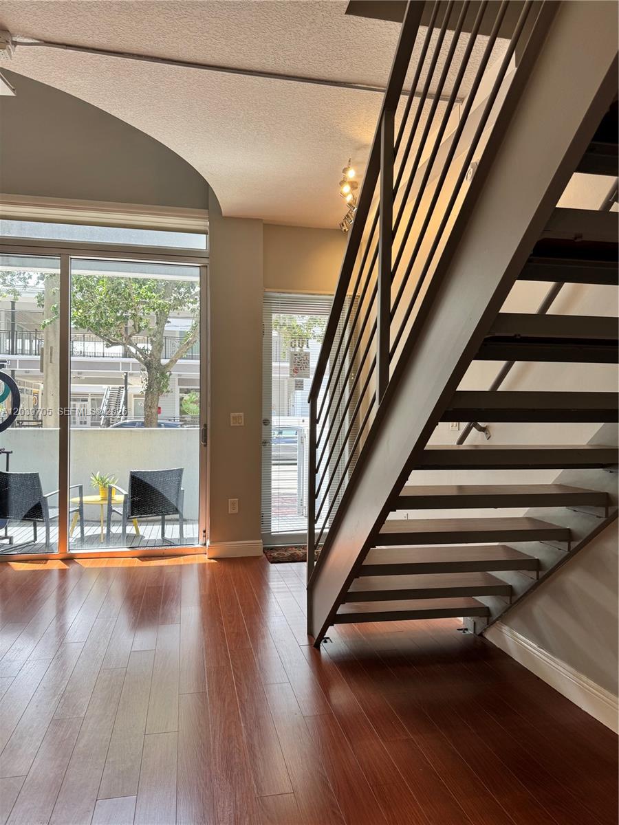 A room with hardwood floors, a metal staircase, and a sliding glass door to a balcony — 3339 Virginia St # 105, Miami FL 33133, MIAMI, FL