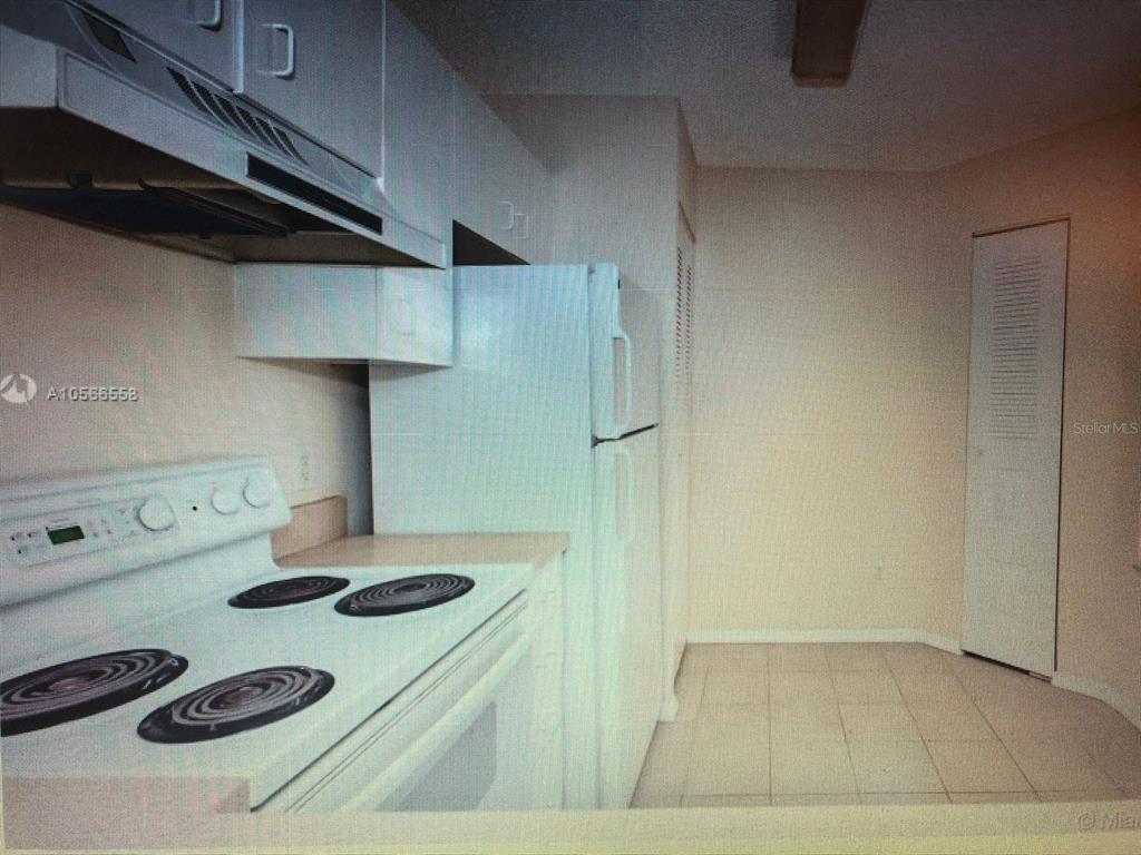 A kitchen features white appliances, white cabinets, and light-colored tile flooring — 1040 CORAL SPRINGS CLUB UNIT 1040, CORAL SPRINGS, FL