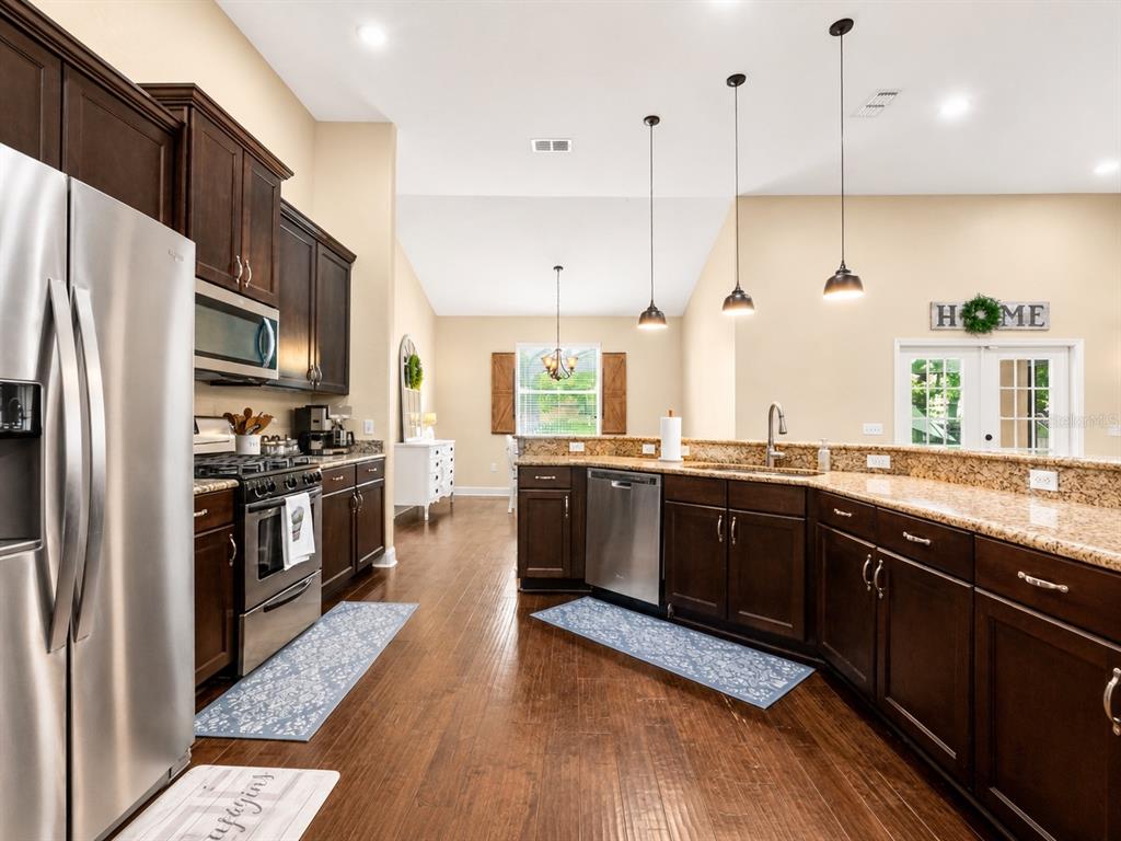 A kitchen features dark wood cabinets, granite countertops, stainless steel appliances, and hardwood flooring — 1939 GRIFFIN TRAIL, BARTOW, FL
