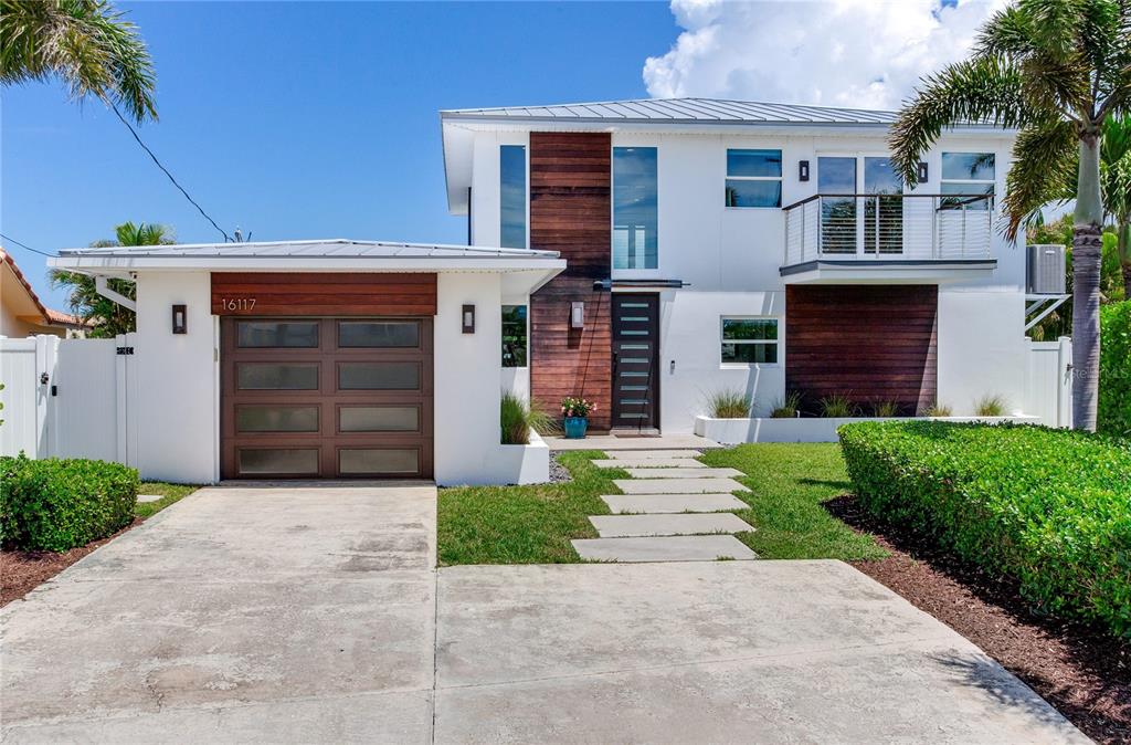 A modern two-story house features white stucco walls, wood paneling, and a single-car garage — 16117 4TH STREET E, REDINGTON BEACH, FL