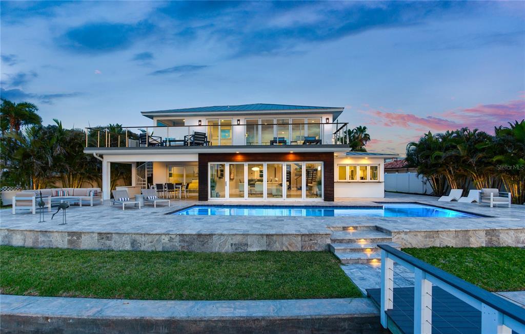 A two-story house with a balcony, swimming pool, and stone patio at sunset — 16117 4TH STREET E, REDINGTON BEACH, FL