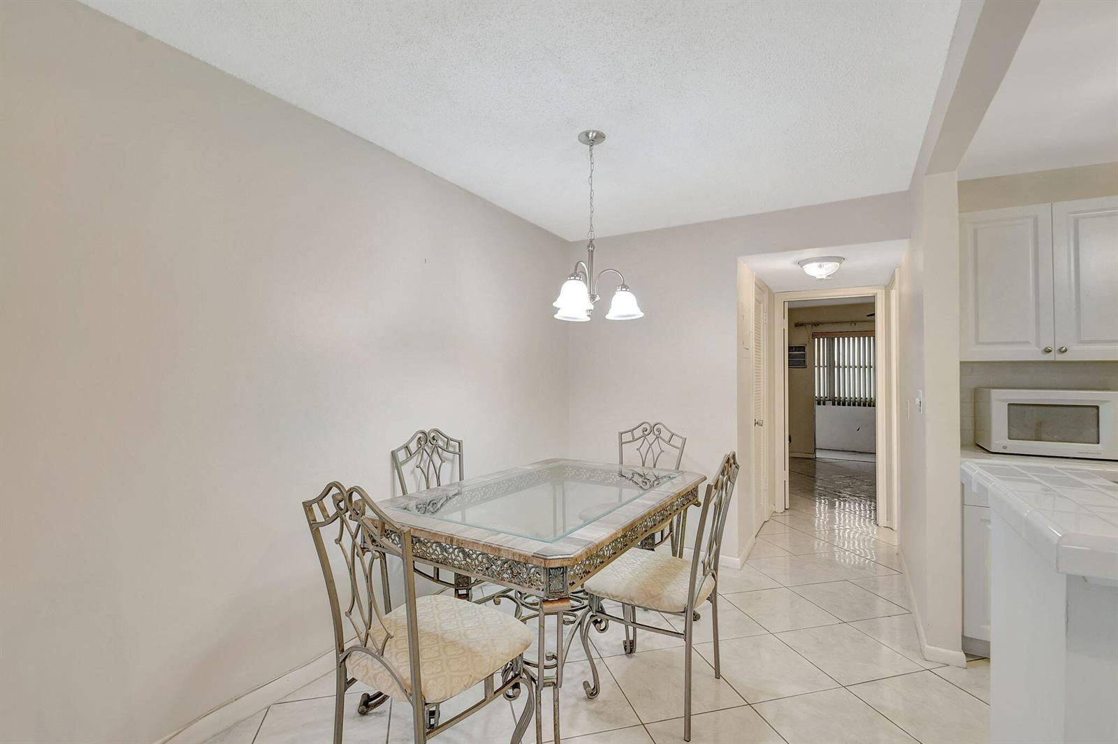 A dining area features a glass-topped table with metal chairs and tile flooring — 70 Camden C, West Palm Beach FL 33417, WEST PALM BEACH, FL