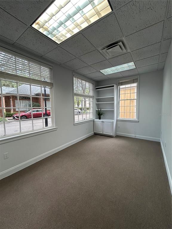 An office space features gray carpet, white walls, large windows, and a built-in shelving unit — 5216 SW 91ST TERRACE UNIT A106, GAINESVILLE, FL