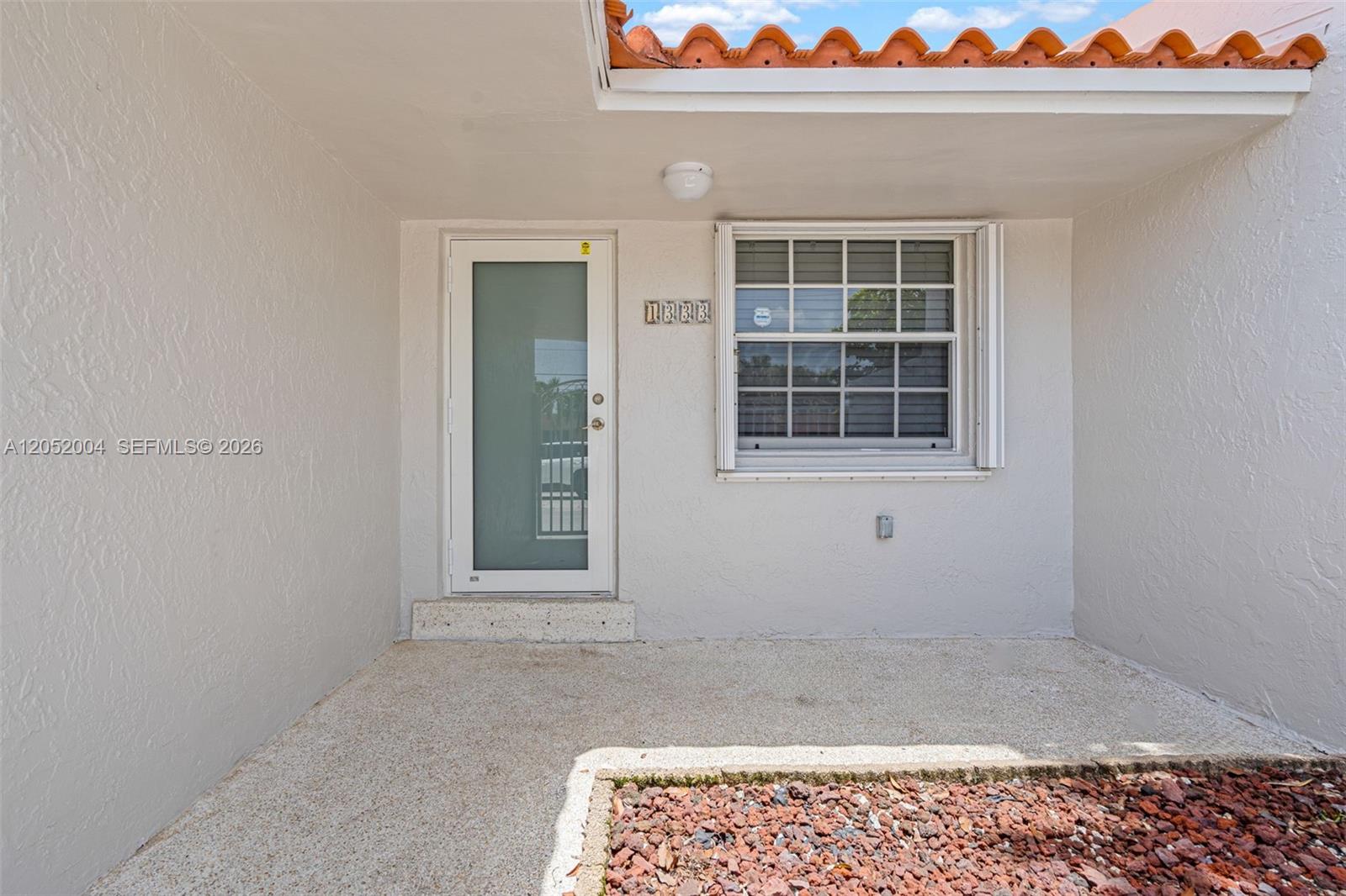 The exterior view shows a white stucco entryway with a glass door and a window — 1333 W 37th St, Hialeah FL 33012, HIALEAH, FL