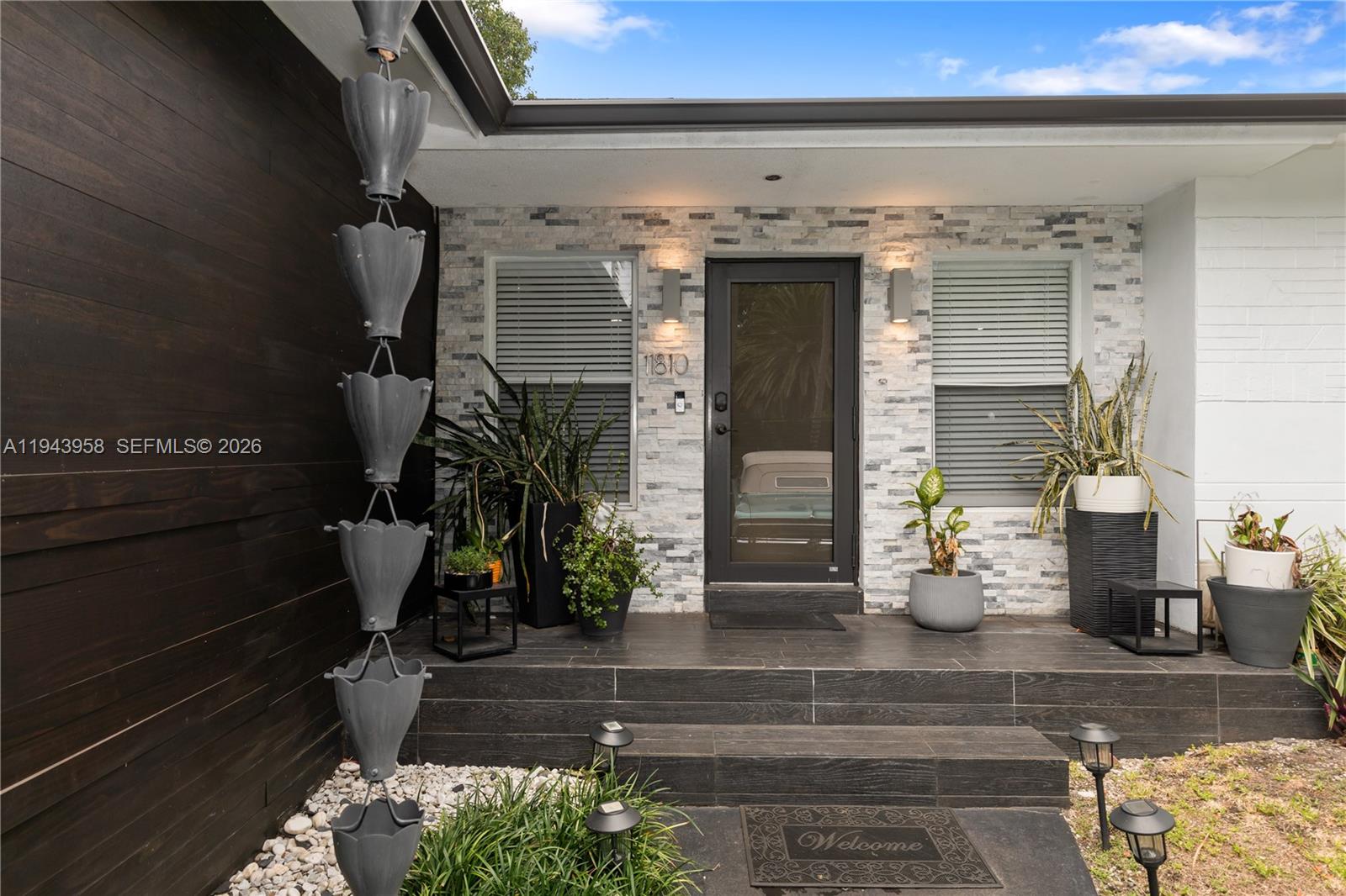 The exterior entrance features a stone-tiled wall, a dark door, and a metal rain chain — 11810 W Biscayne Canal Rd, Miami FL 33161, MIAMI, FL