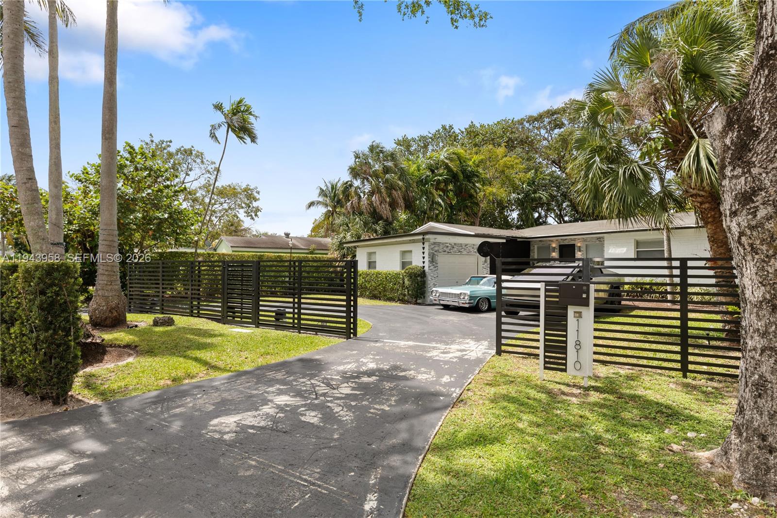 A single-story house with a driveway, black horizontal fencing, and a vintage car parked outside — 11810 W Biscayne Canal Rd, Miami FL 33161, MIAMI, FL