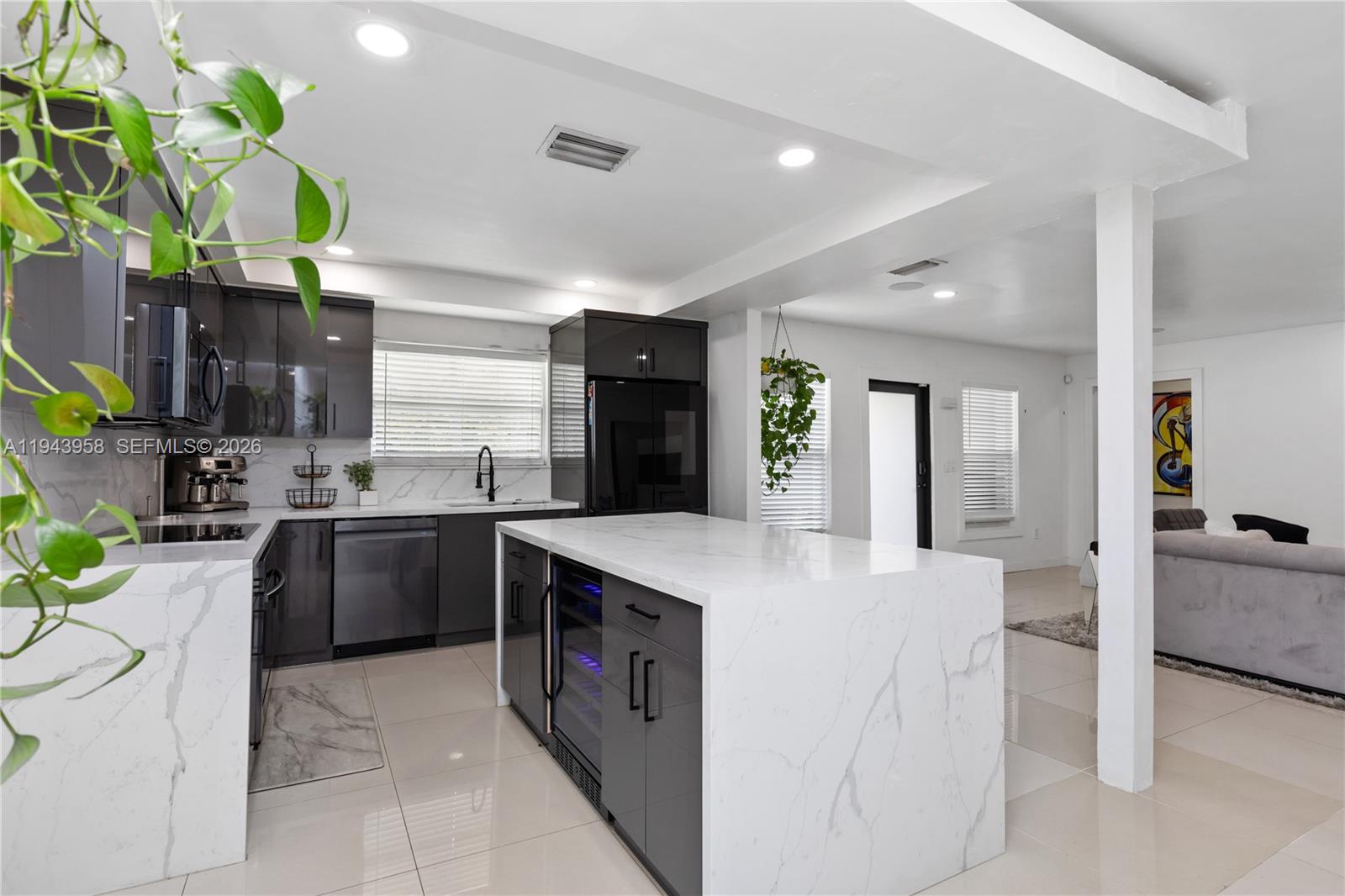 A modern kitchen features dark gray cabinetry, a marble waterfall island, and light tile flooring — 11810 W Biscayne Canal Rd, Miami FL 33161, MIAMI, FL