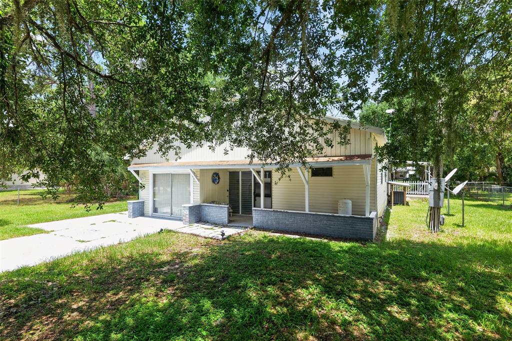 A light-colored house with a covered patio and brick base sits in a grassy yard — 10513 LYNNWOOD AVENUE, LAKE WALES, FL