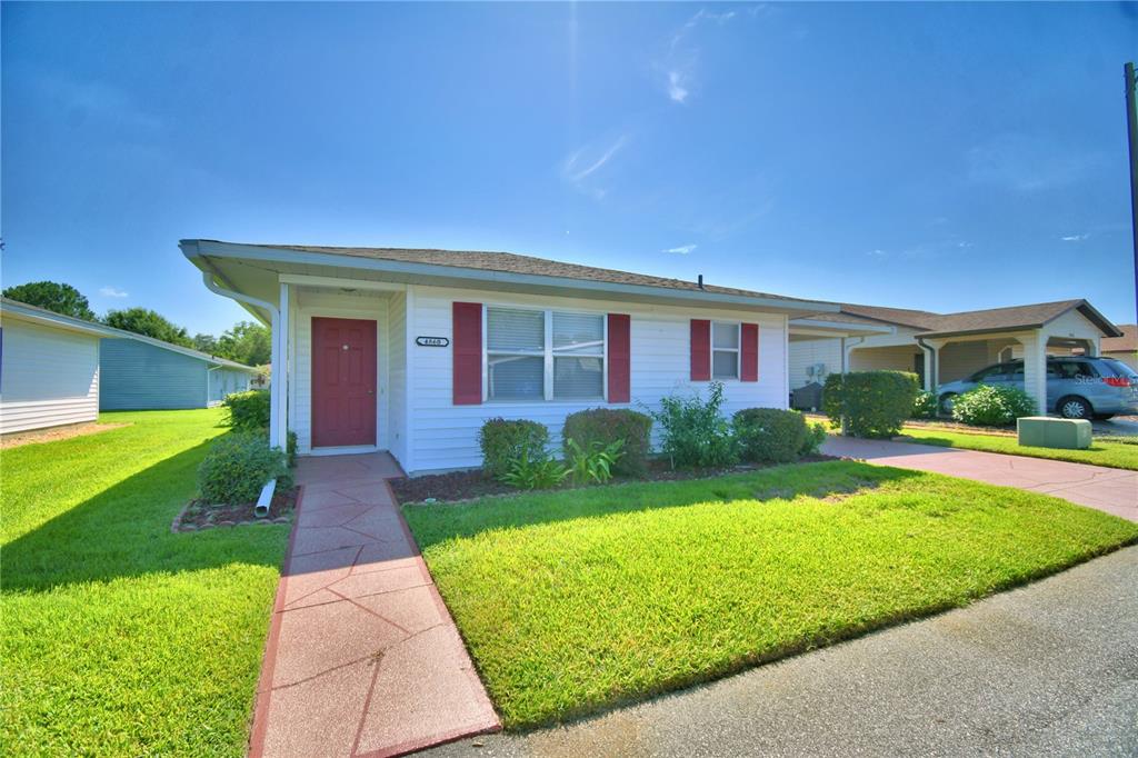 A single-story white house with a red front door and a paved walkway — 4860 GOLDENVIEW LANE, LAKELAND, FL