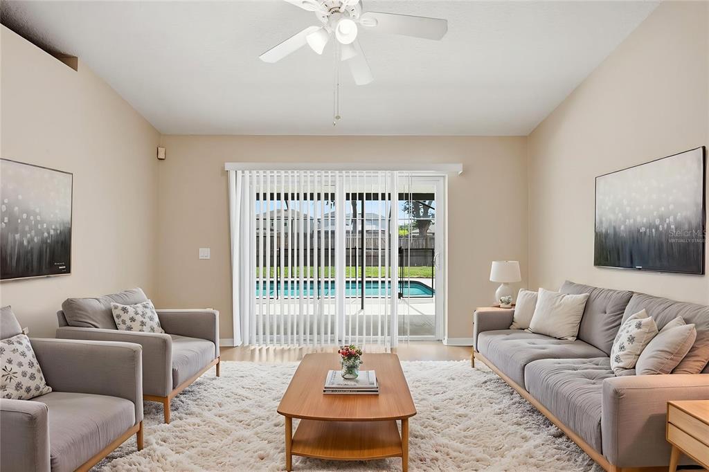 A living room features gray sofas, a wood coffee table, and a sliding door to a pool — 3049 CASTLE ROCK CIRCLE, LAND O LAKES, FL