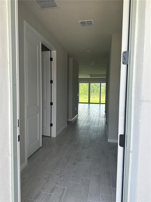A view from a doorway looking down a hallway with gray tile flooring toward windows — 17663 SAW PALMETTO AVENUE, CLERMONT, FL