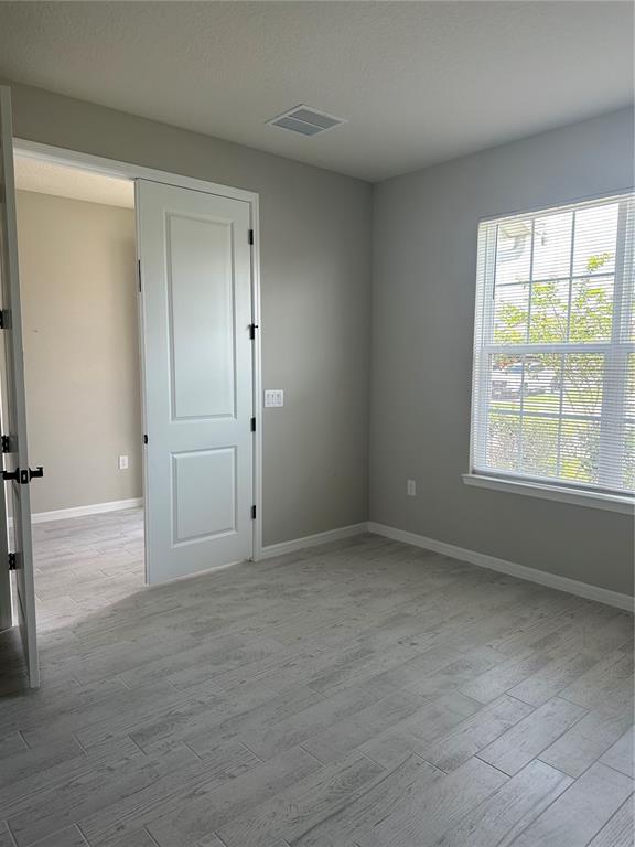 An empty room features light gray walls, wood-look tile flooring, and a window with blinds — 17663 SAW PALMETTO AVENUE, CLERMONT, FL