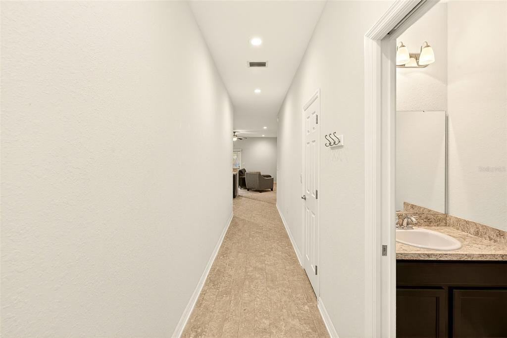 A hallway with carpeted flooring leads to a living area, with a bathroom entrance adjacent — 4680 VIGNETTE WAY, SARASOTA, FL