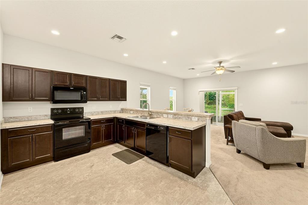 A kitchen with dark wood cabinets and black appliances opens into a carpeted living area — 4680 VIGNETTE WAY, SARASOTA, FL
