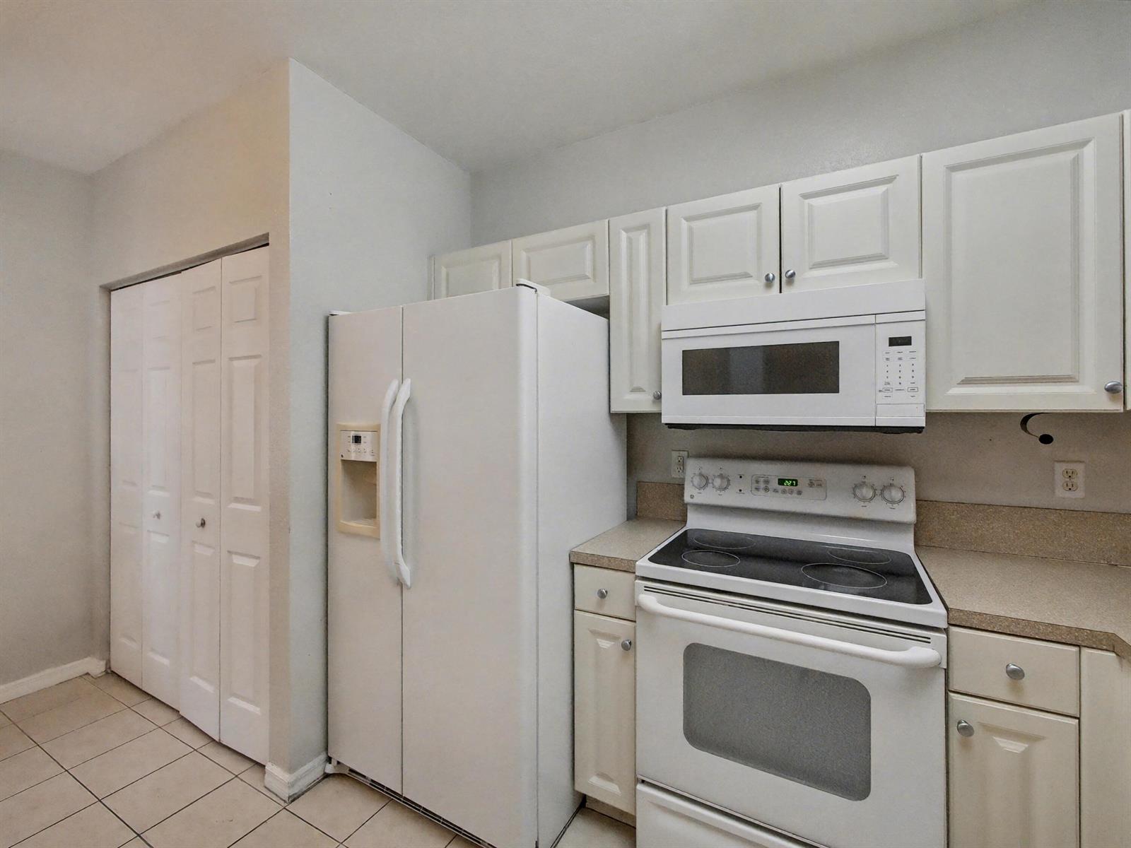 A kitchen features white cabinets, a white refrigerator, a microwave, and a white electric stove — 3425 Sonoma Drive, Riviera Beach FL 33404, RIVIERA BEACH, FL