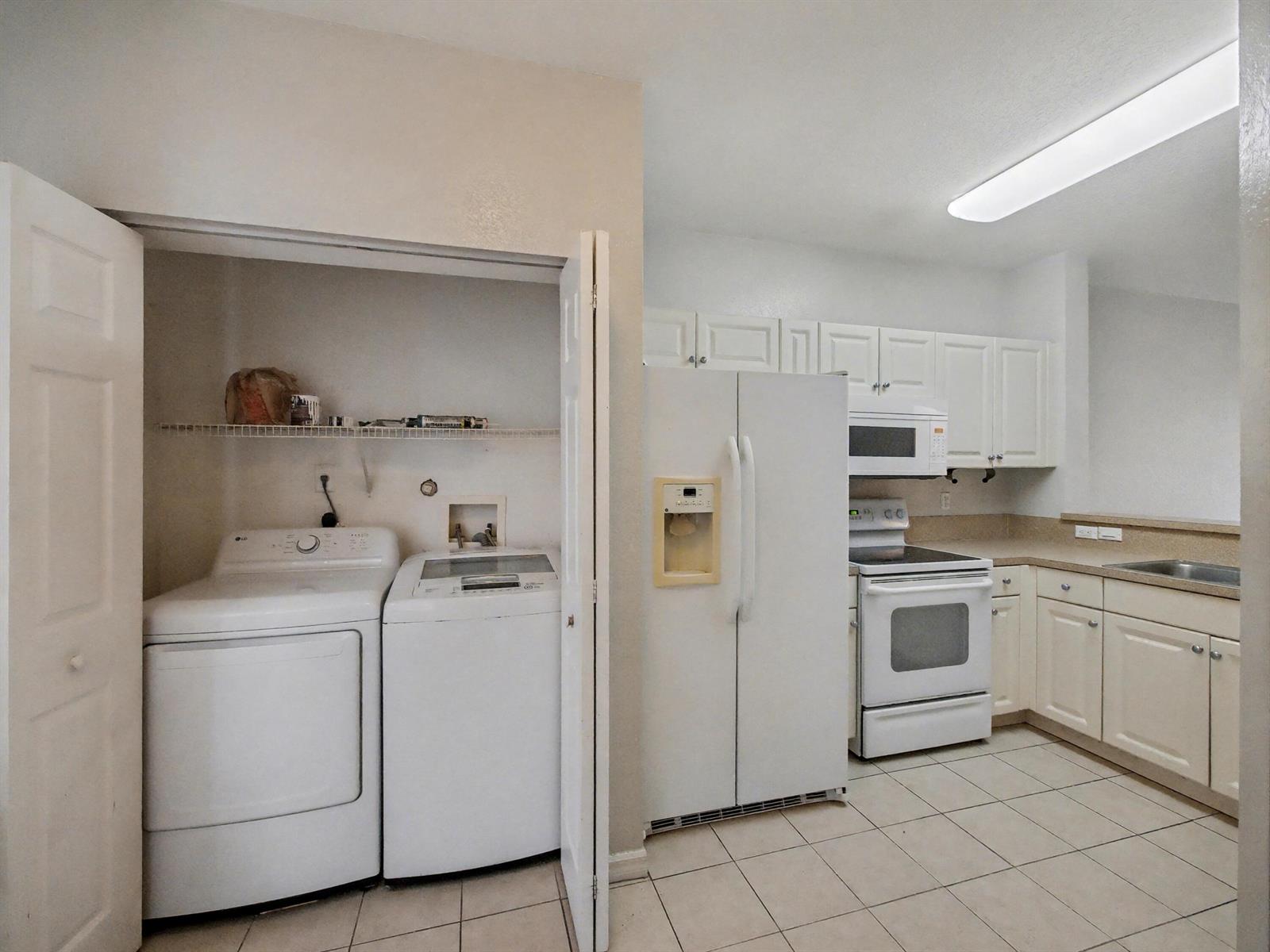 A kitchen with white cabinets and appliances next to a laundry closet with a washer-dryer — 3425 Sonoma Drive, Riviera Beach FL 33404, RIVIERA BEACH, FL