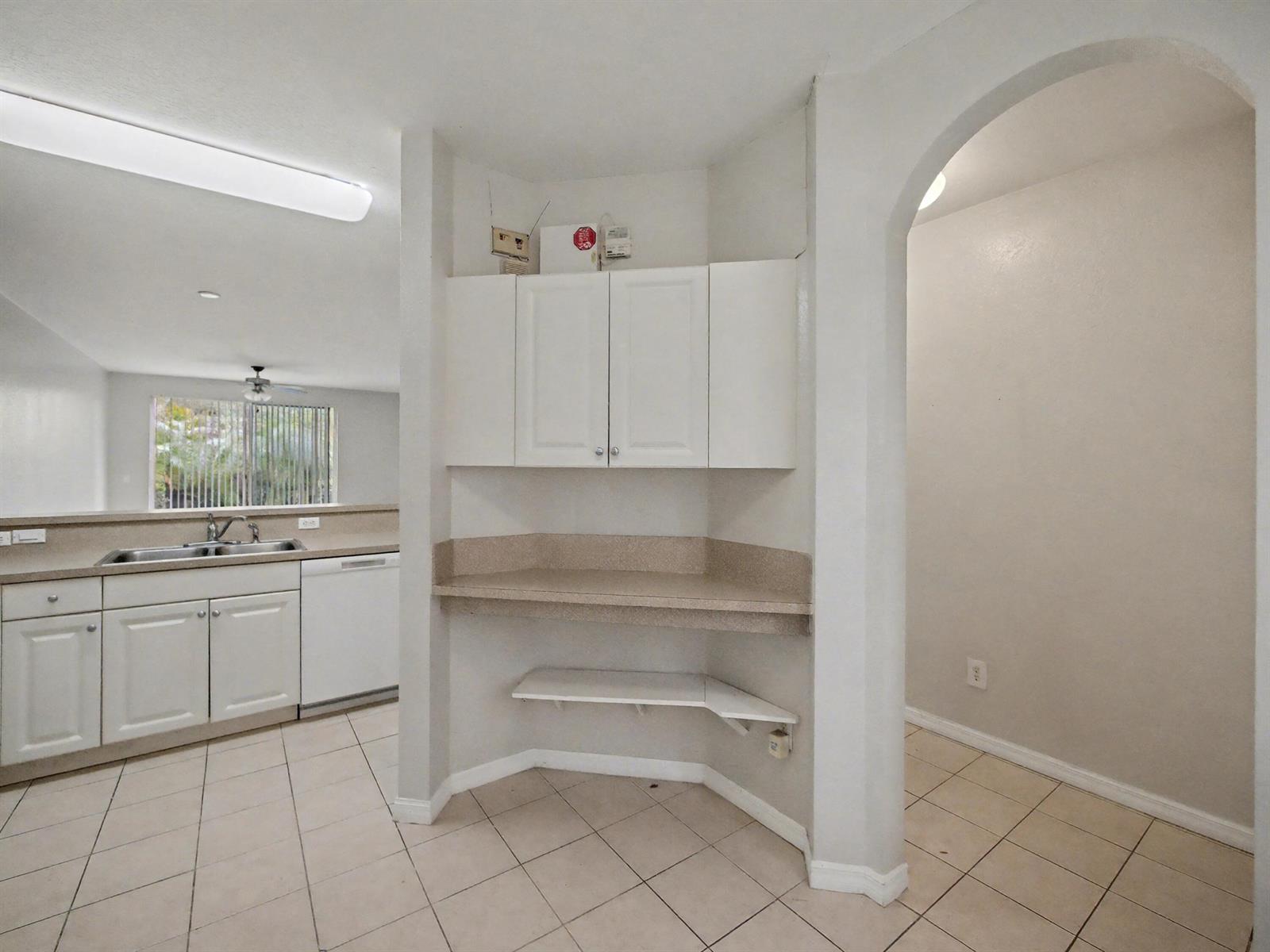 A kitchen features white cabinets, a corner desk area, and light-colored tile flooring — 3425 Sonoma Drive, Riviera Beach FL 33404, RIVIERA BEACH, FL