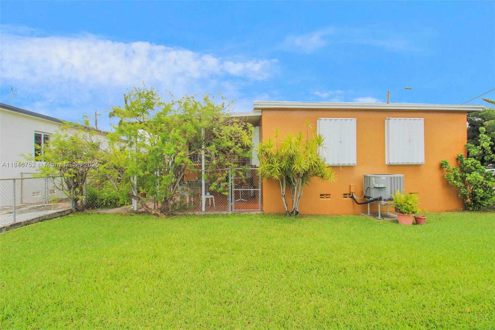 The exterior of an orange house features a fenced patio area and a grassy lawn — 3600 NW 19th Ter, Miami FL 33125, MIAMI, FL