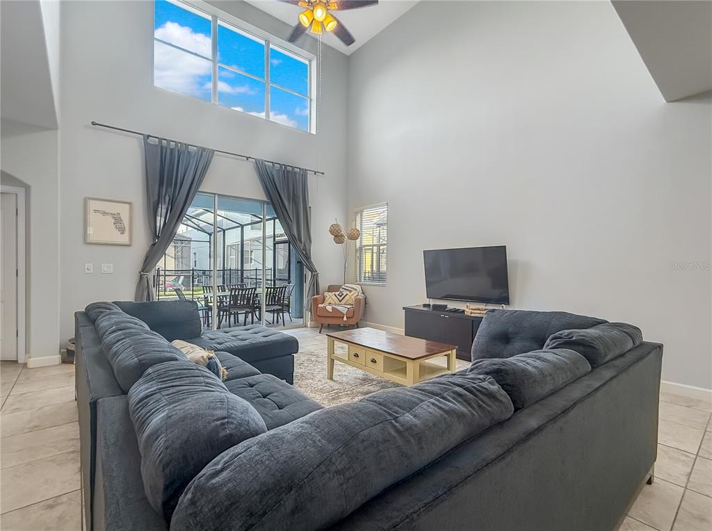 A living room features a large sectional sofa, high ceilings, and a view of a patio — 2942 BUCCANEER PALM ROAD, KISSIMMEE, FL
