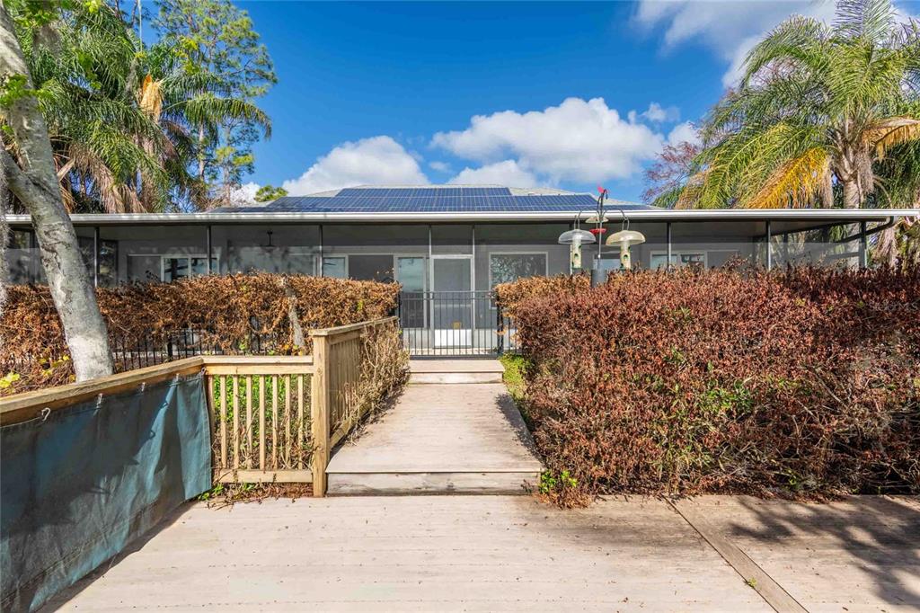 A wooden walkway leads to a screened-in patio with solar panels on the roof — 6716 MAGNOLIA POINT DRIVE, LAND O LAKES, FL