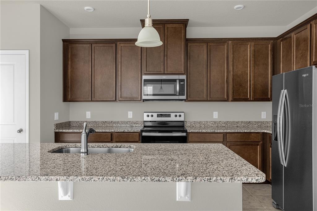 A kitchen features dark wood cabinets, granite countertops, a stainless steel microwave, and a sink — 1926 HOLDEN RIDGE LANE, CLERMONT, FL