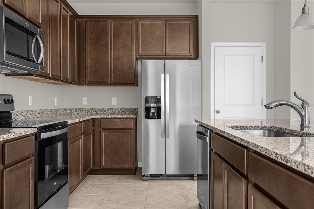 A kitchen features dark wood cabinets, granite countertops, stainless steel appliances, and tile flooring — 1926 HOLDEN RIDGE LANE, CLERMONT, FL