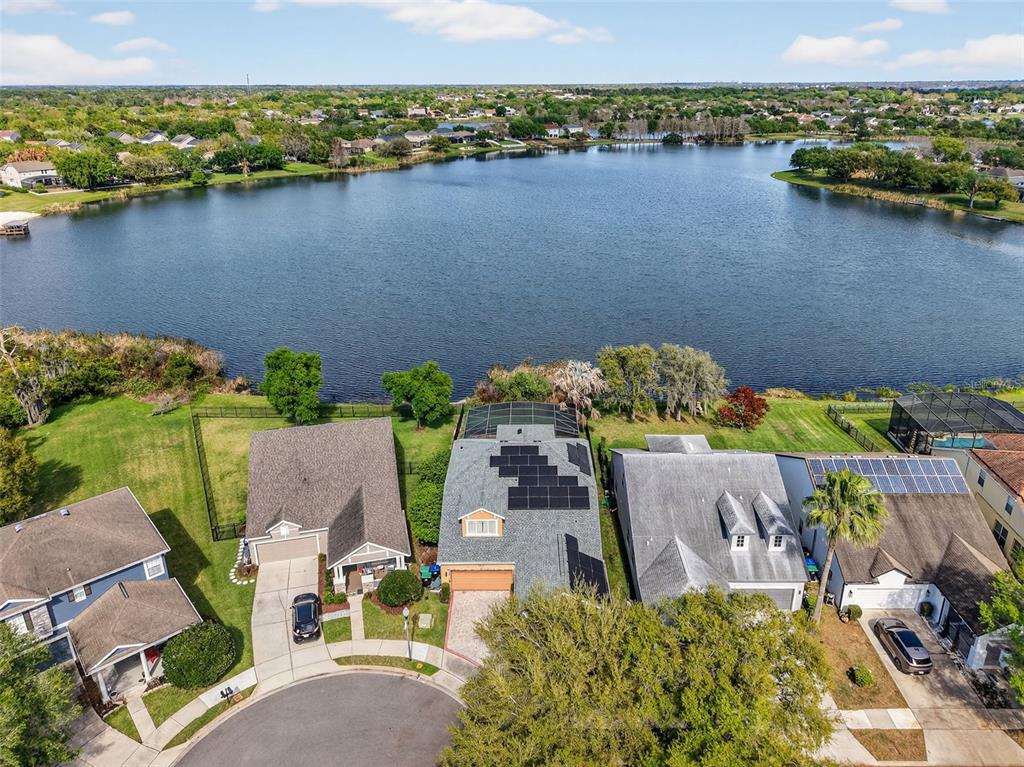 An aerial view shows suburban houses with solar panels and screened pools bordering a large lake — 5413 WALSH POND COURT, WINDERMERE, FL