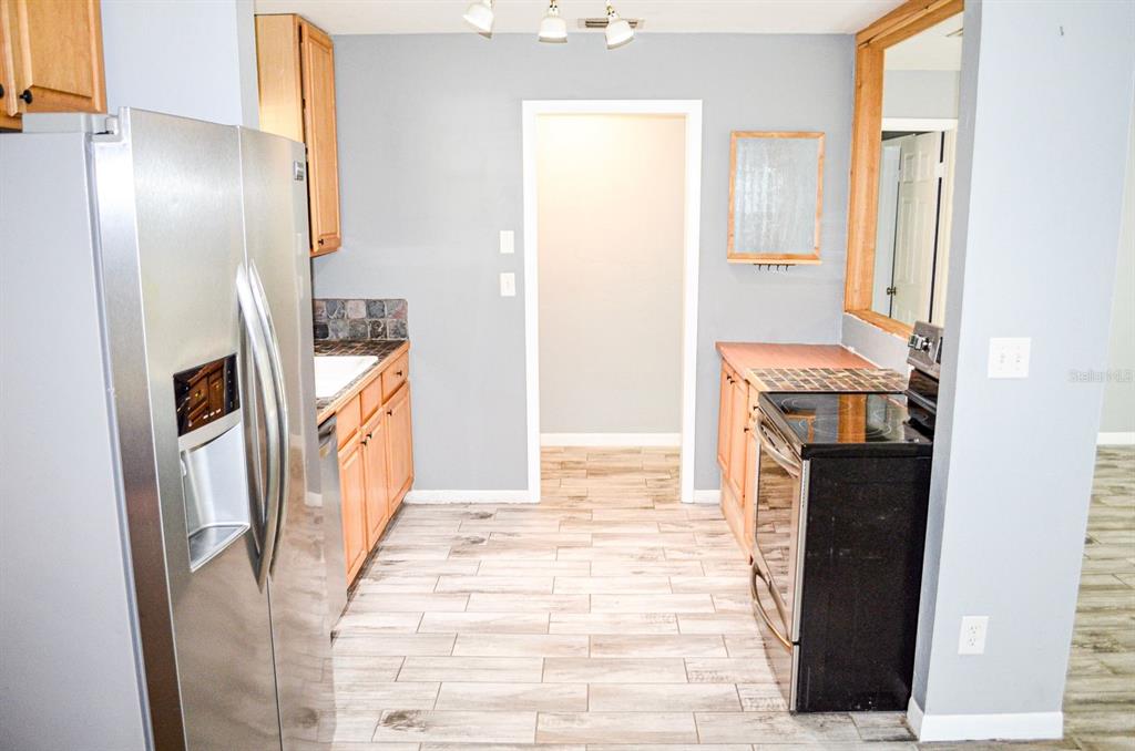 A kitchen features light wood cabinets, stainless steel appliances, and light-colored wood-look tile flooring — 3526 NW 53RD TERRACE, GAINESVILLE, FL